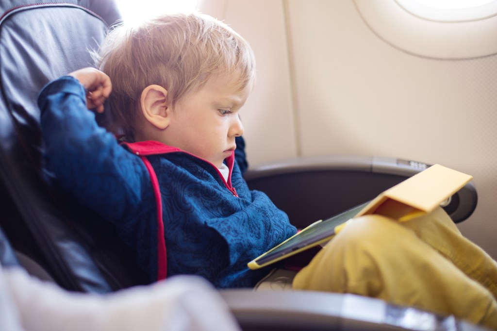 Little boy sitting on an airplane seat crying while using a tablet